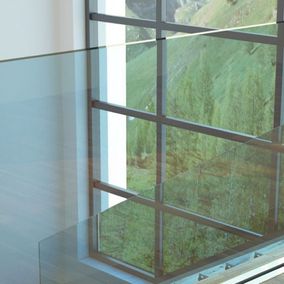 Detailansicht eines Fensters mit Metallrahmen und Unterteilungen. Der Blick geht durch blaue Glasscheiben auf dieses Fenster.