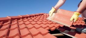 Detailansicht eines roten Ziegeldaches, wo ein Handwerker einen Ziegel gerade einsetzt.