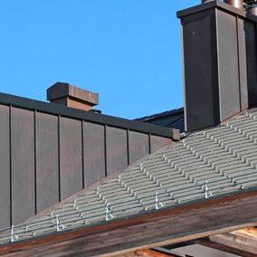 Detailansicht eines Daches mit Metall verblendeten Schornsteinen und eines hervorstehenden Fensters.
