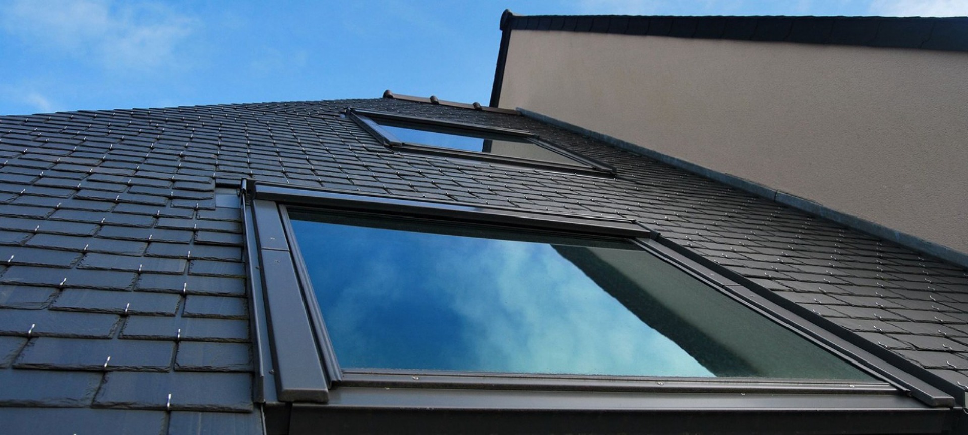 Detailansicht von zwei Dachfenstern auf einem schwarz gedecktem Dach.