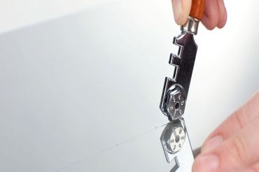 Detailansicht einer Glasscheibe, wo eine Hand mit einem Glasschneider eine Linie entlangfährt